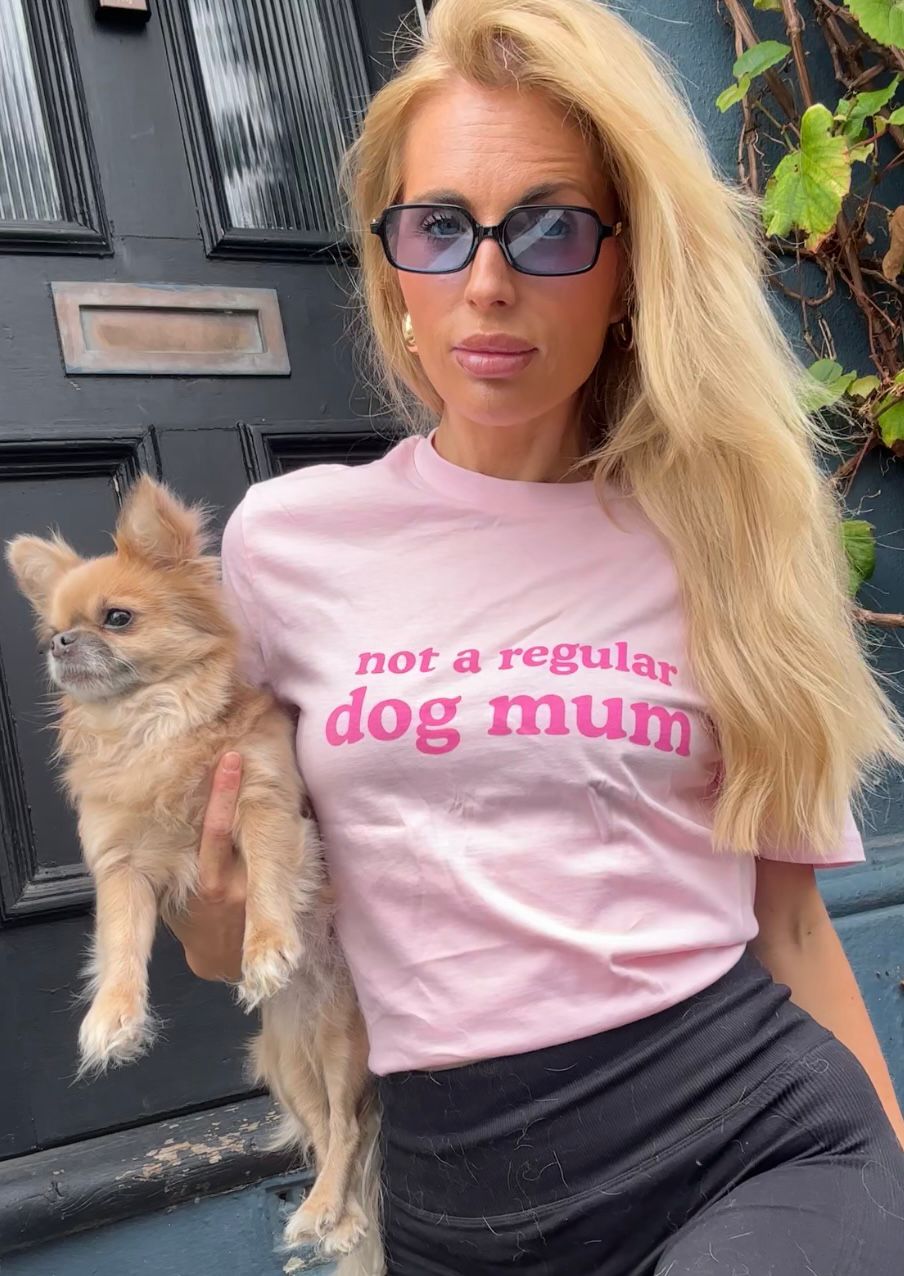 Front view of a customer wearing the pink Not a Regular Dog Mum tee and holding a small tan dog.