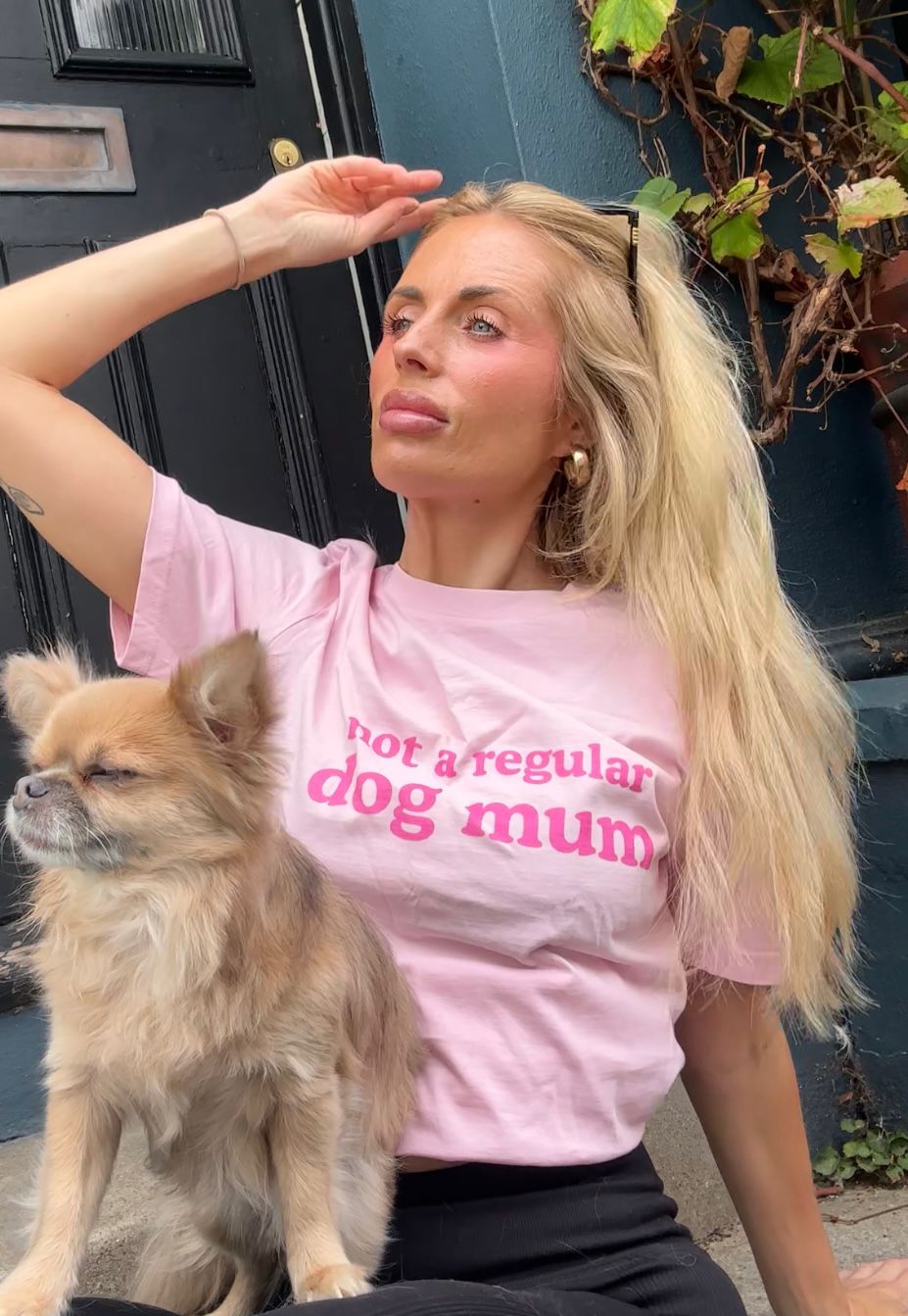 A customer seated outside in the pink Not a Regular Dog Mum tee with a small tan dog on her lap.