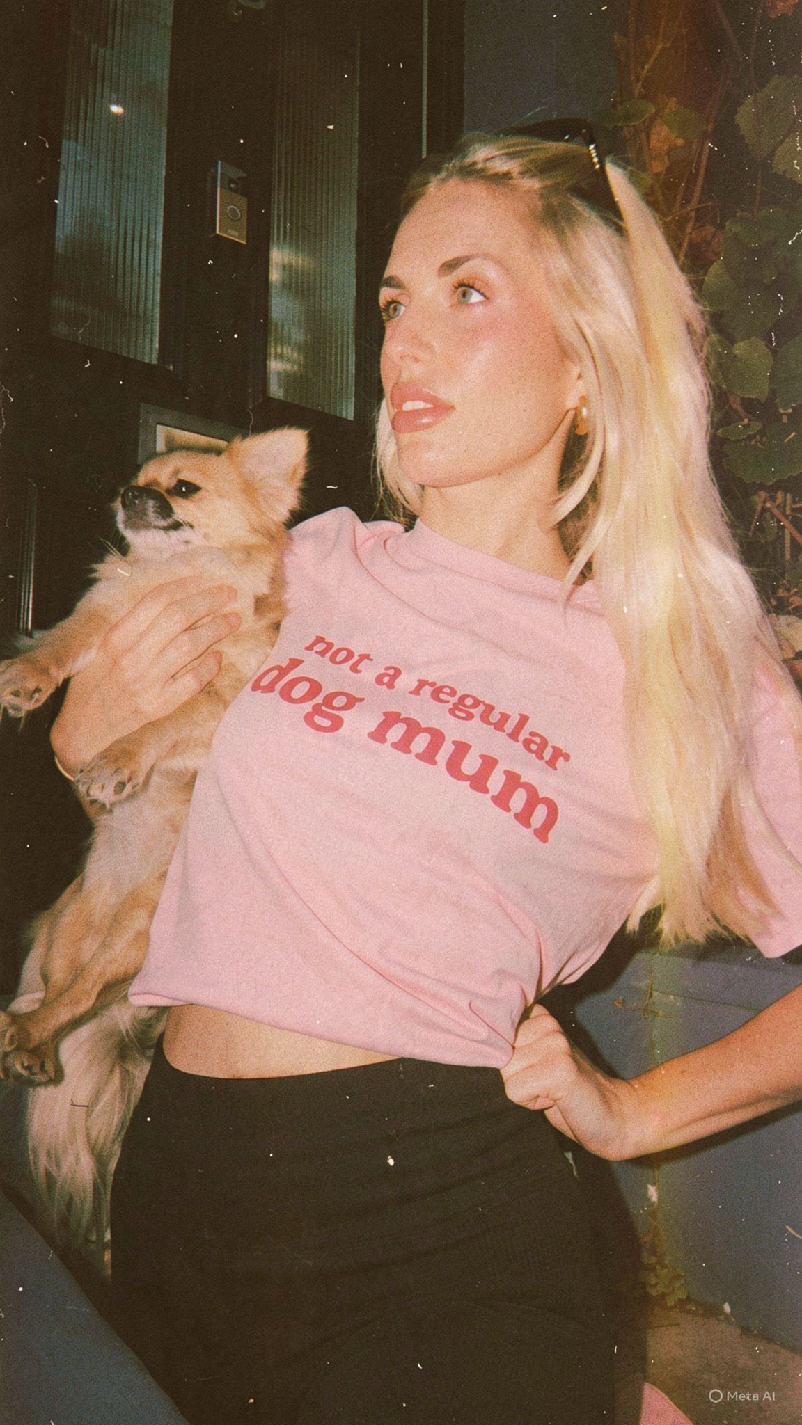 A vintage-style photo of a customer wearing the pink Not a Regular Dog Mum tee while holding a small tan dog.