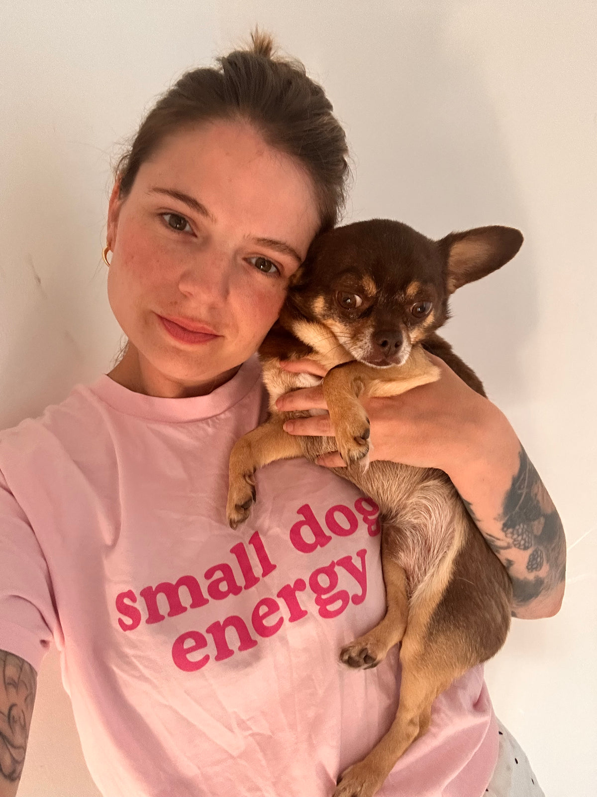 A customer wearing the pink small dog energy tee while holding a brown Chihuahua.