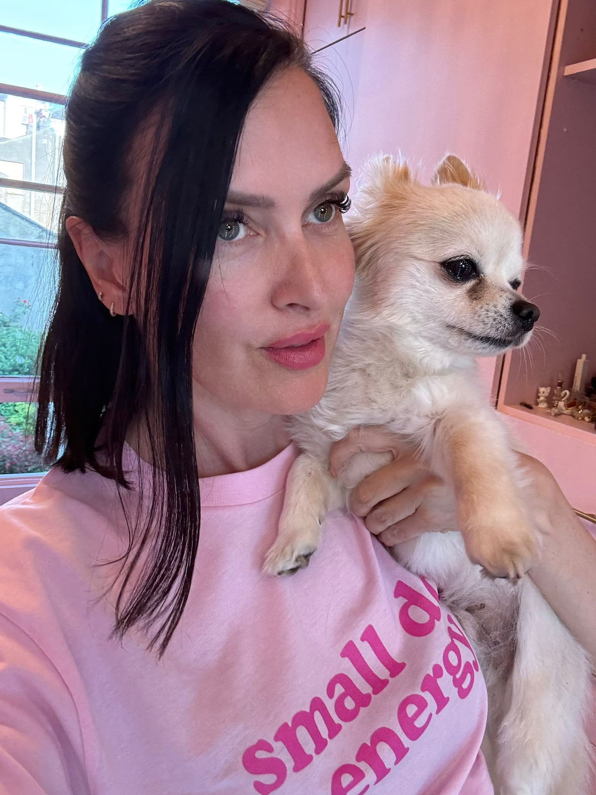 A customer wearing the pink small dog energy tee while holding a cream Chihuahua.