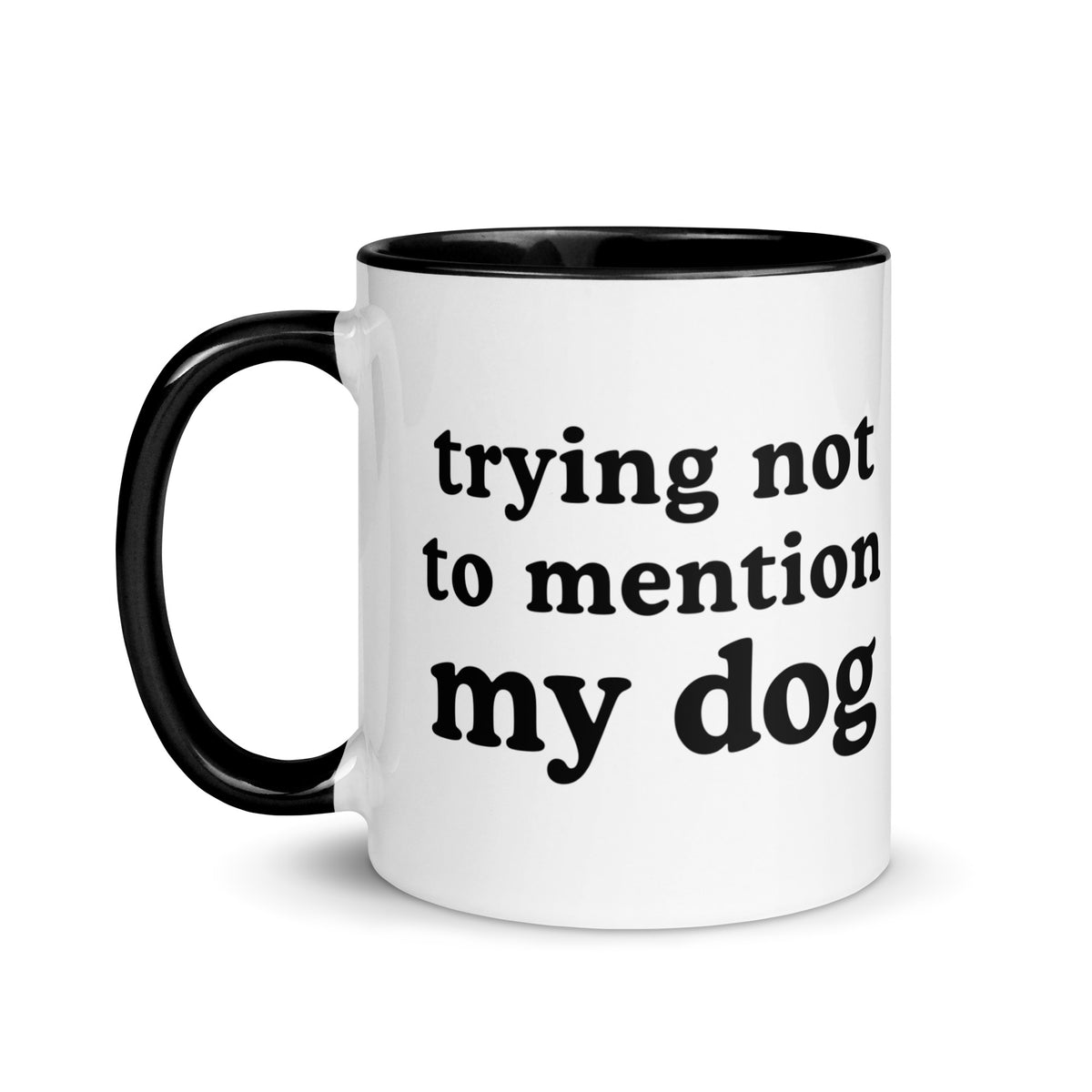 A white ceramic coffee mug with a black handle, black interior, and black printed text reading 'trying not to mention my dog' on a clean white background.