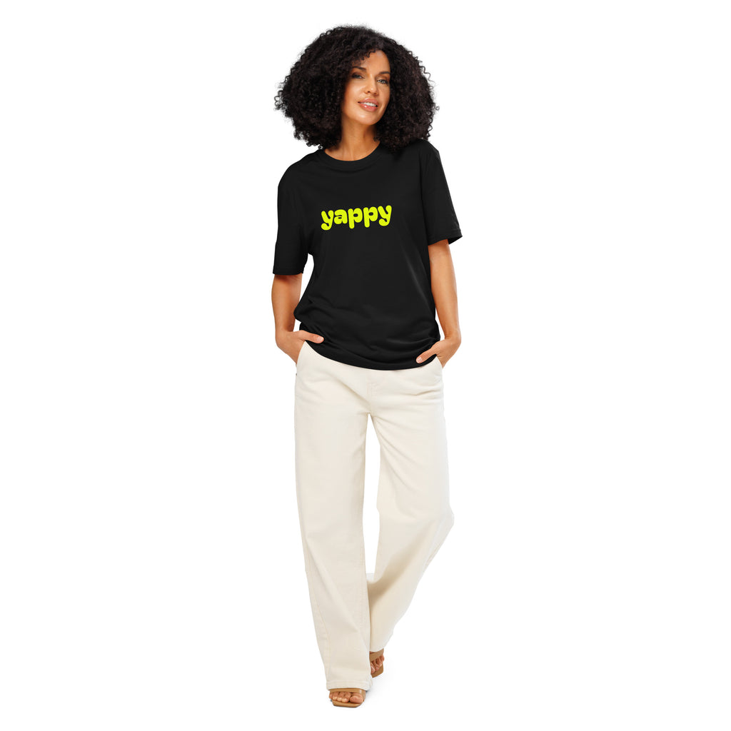 Woman wearing a black t-shirt with yellow text that says yappy and white pants on a white background